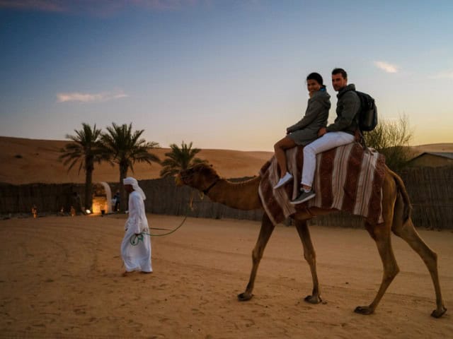 A picture of a man leading people on a camel through a camel ride in the desert.