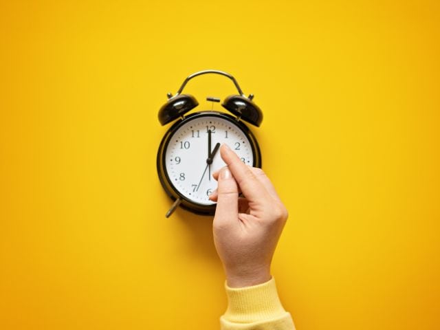 A person trying to move the hands of a clock which indicates saving time.