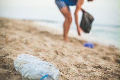 A picture of a woman volunteering and cleaning a beach by picking plastic bottles and waste.