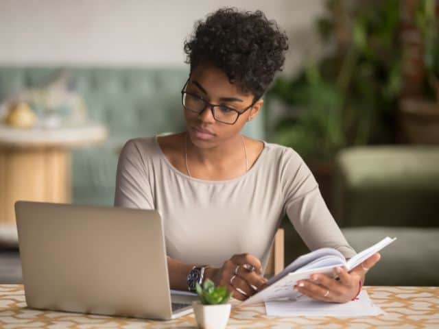 A picture of a woman doing research and taking notes in a notebook.