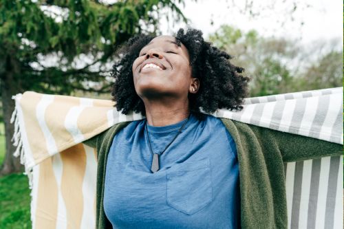 A picture of a black woman outside smiling and looking happy with her eyes closed.