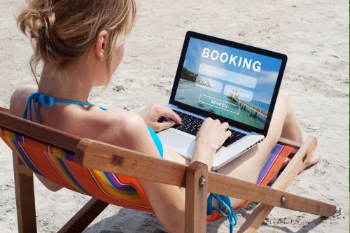 A picture of a woman sitting on a chair in sand and using her laptop to book tours.