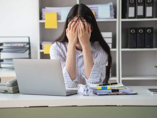 A picture of a woman covering her face with her hand to indicate burnout.