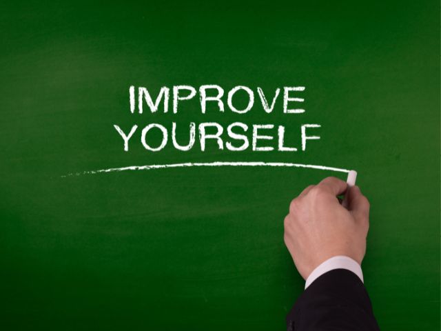 A picture of a person writing the phrase "improve yourself" on a board.