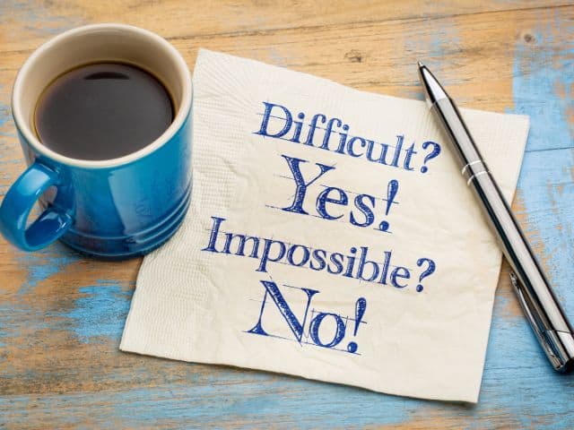 A picture of the sentence "Difficult? Yes! Impossible? No!" written on a napkin next to a cup pf espresso.