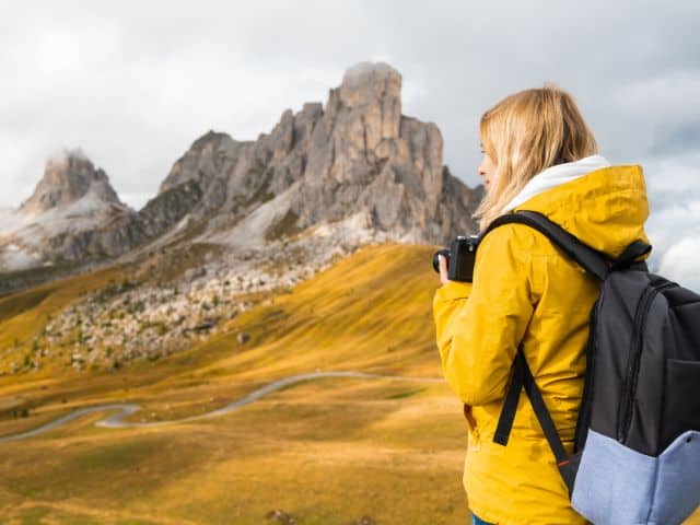 A picture of a female photographer in a yellow jacket taking pictures of mountains.