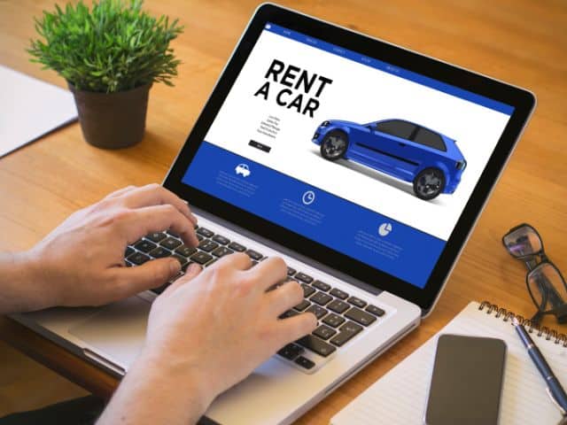 A picture of a man using a laptop to rent a car online.