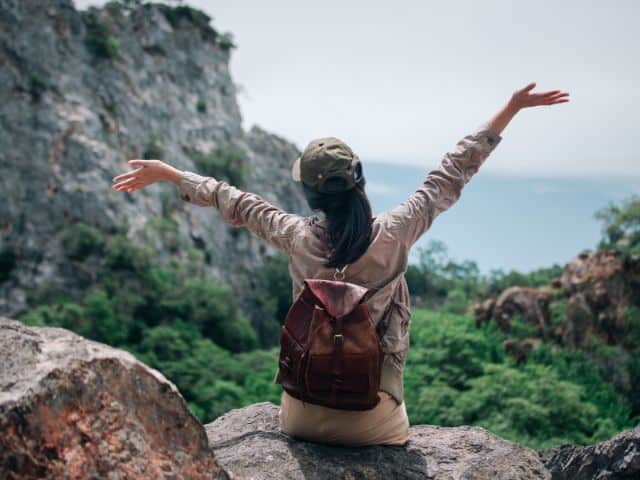 A picture of a woman traveling on her own and sitting on a cliff.