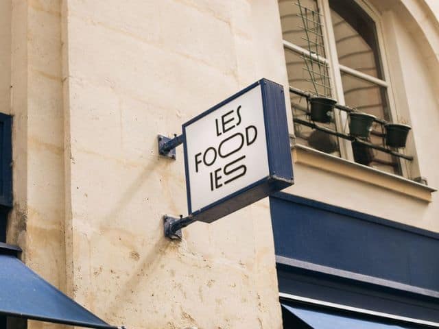 A picture of a sign outside of Les Foodies restaurant in Paris, France with the name of the restaurant written on it. 