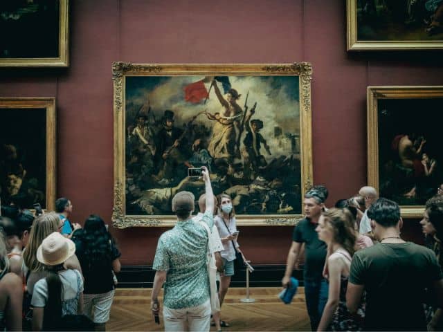 A picture of people looking at a painting inside of the Louvre Museum in Paris, France.