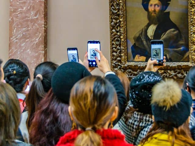 A picture of a group of people taking photos of Portrait of Baldassare Castiglione inside of the Louvre Museum in Paris, France.