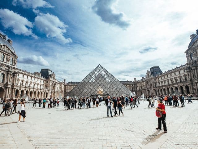 A picture of people walking outside of the Louvre Museum in Paris, France.