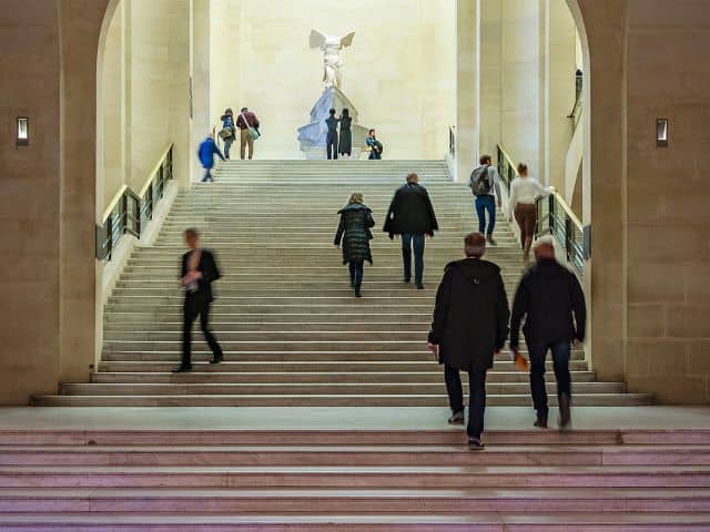 A picture of people walking up the stairs in the Louvre Museum in Paris, France.