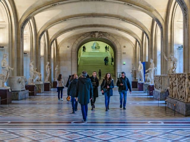 A picture of several people walking inside of the Louvre Museum in Paris, France.