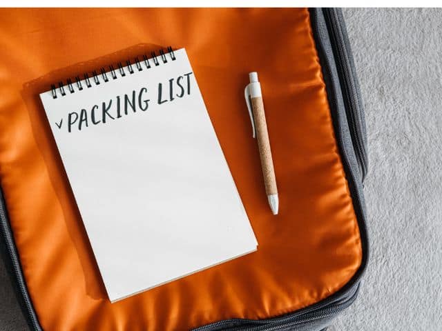 A picture of the words "PACKING LIST" written on a notebook that is inside an orange bag.