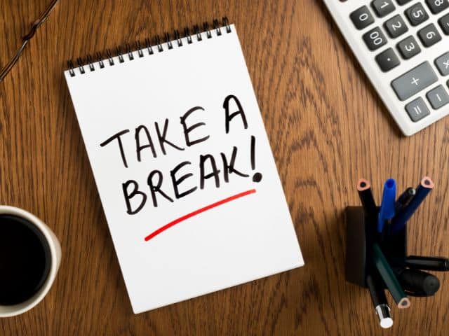 A picture of the words "TAKE A BREAK" written on a white notepad placed on an office desk.