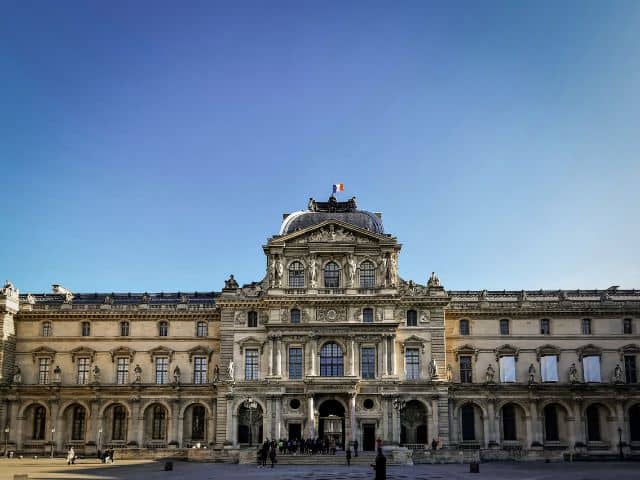 A picture outside of the Louvre Museum highlighting its large size.