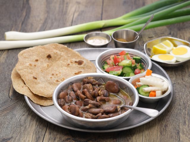 A picture of a food tray filled with plates of fuul, salad, and eggs.