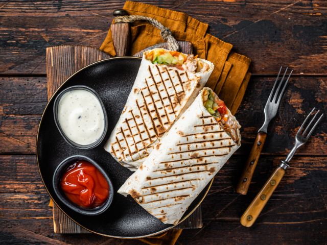 A picture of shawarma sandwiches in a plate placed on a wooden background.