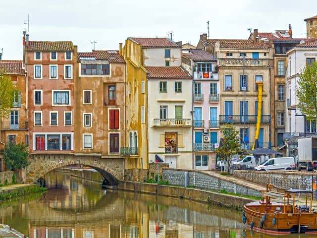 A picture of several colorful houses and a canal in Narbonne, France.