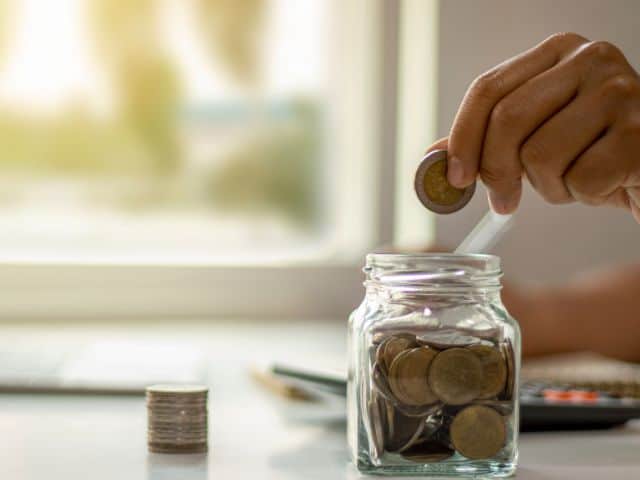 A picture of someone putting money in a glass jar.