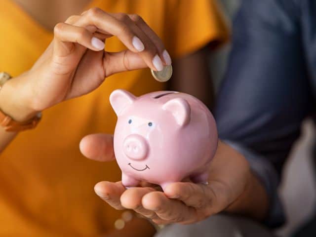 A picture of two people putting a coin in a piggybank.