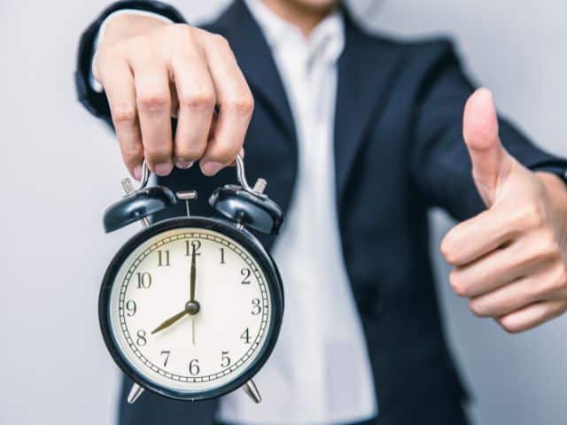 A picture of a man holding an alarm clock and raising his thumb.