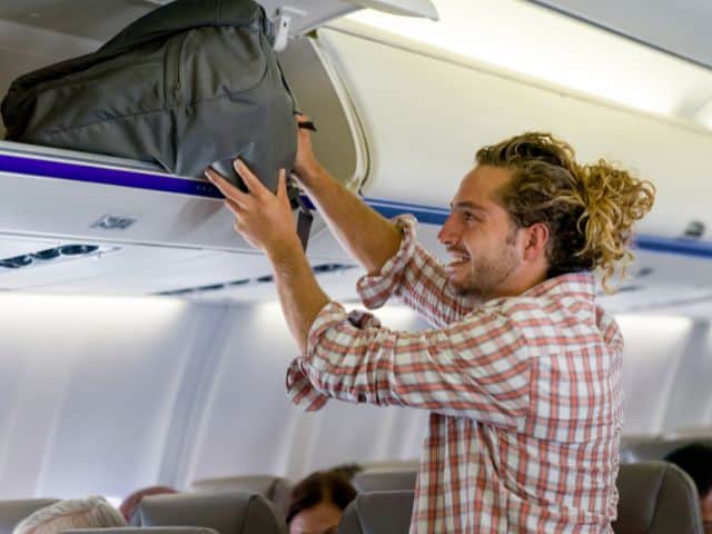 A picture of a passenger putting his carry-on bag into the overhead compartment.