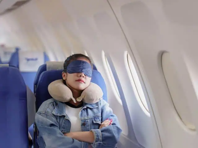 A picture of a woman sleeping and using a pillow inside an airplane.