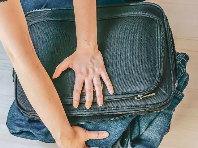 A picture of someone trying to close an overpacked bag.