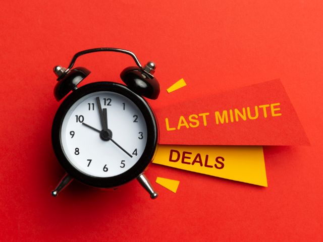 A picture of the words "last minute deals" written on an colored papers next to an alarm clock.